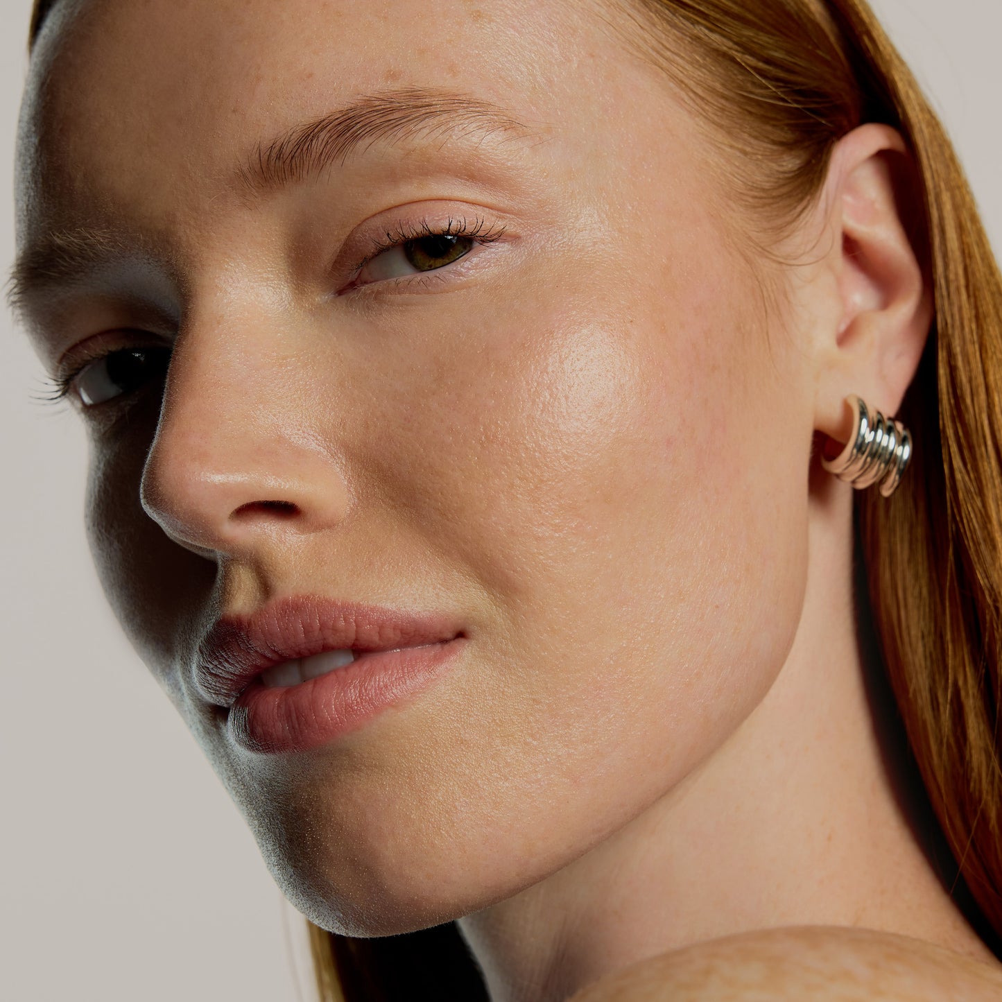 Close-up of a woman's face wearing a silver hoop earring against a neutral background